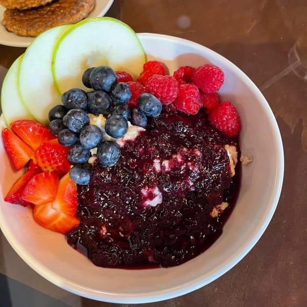 Oatmeal bowl with berry compote, fresh blueberries, raspberries, strawberries, and sliced green apples.