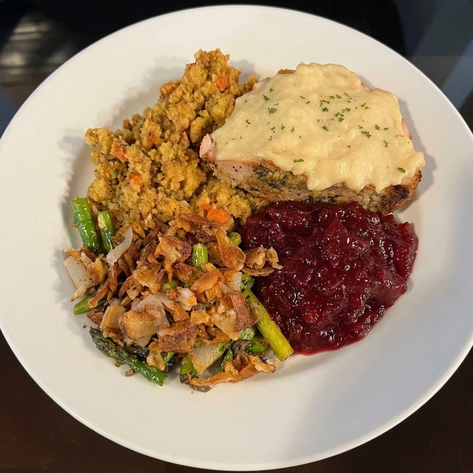 A plate of meatloaf with gravy, stuffing, cranberry sauce, and roasted asparagus with fried onions.