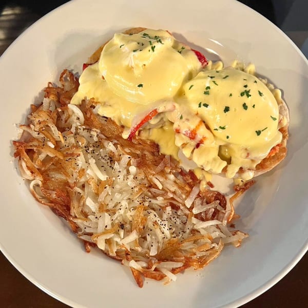 Eggs Benedict with hollandaise sauce and hash browns on a white plate at Whiskey Kitchen Mount Dora.