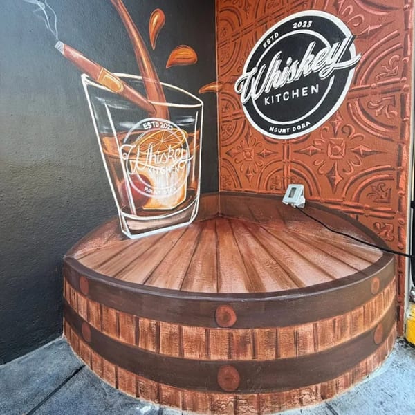 Mural of a whiskey glass with a cigar and orange slice, on a barrel, with the Whiskey Kitchen logo.