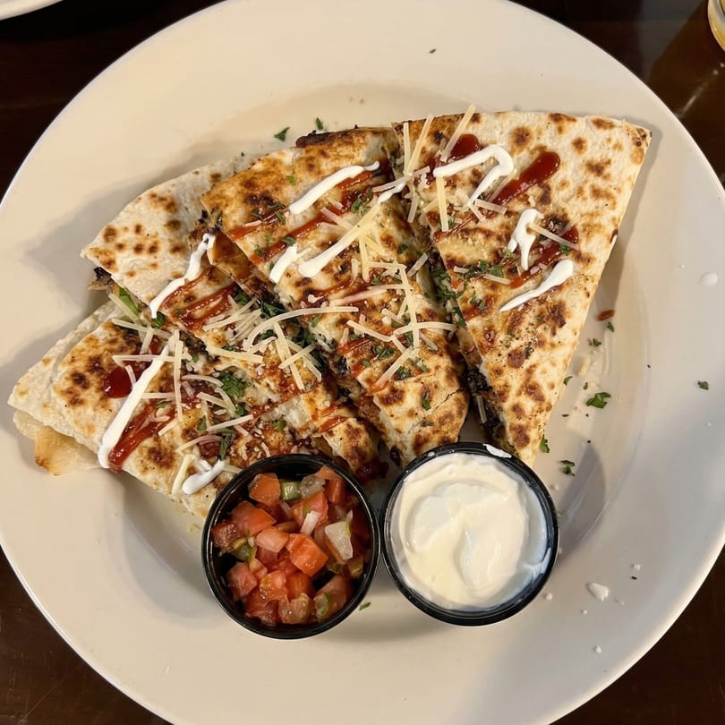 Quesadillas drizzled with white sauce and ketchup, topped with cheese and parsley, served with salsa and sour cream.