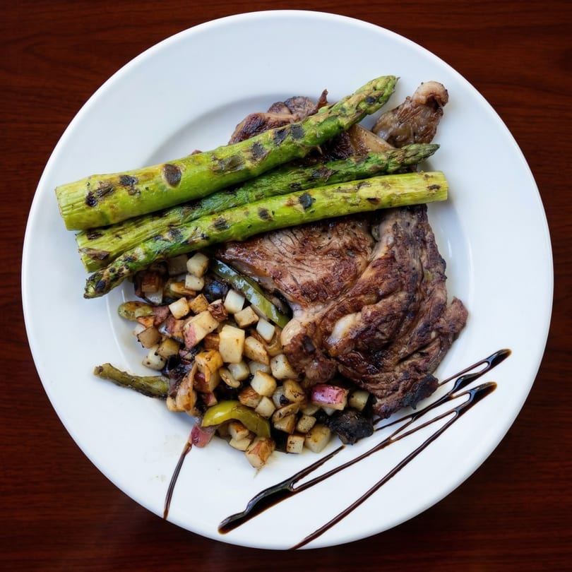 Grilled steak with roasted potatoes, asparagus, and a balsamic glaze on a white plate.