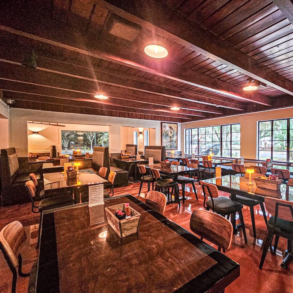 Warmly lit interior of Whiskey Kitchen Mount Dora, featuring dark tables, booths, and large windows.