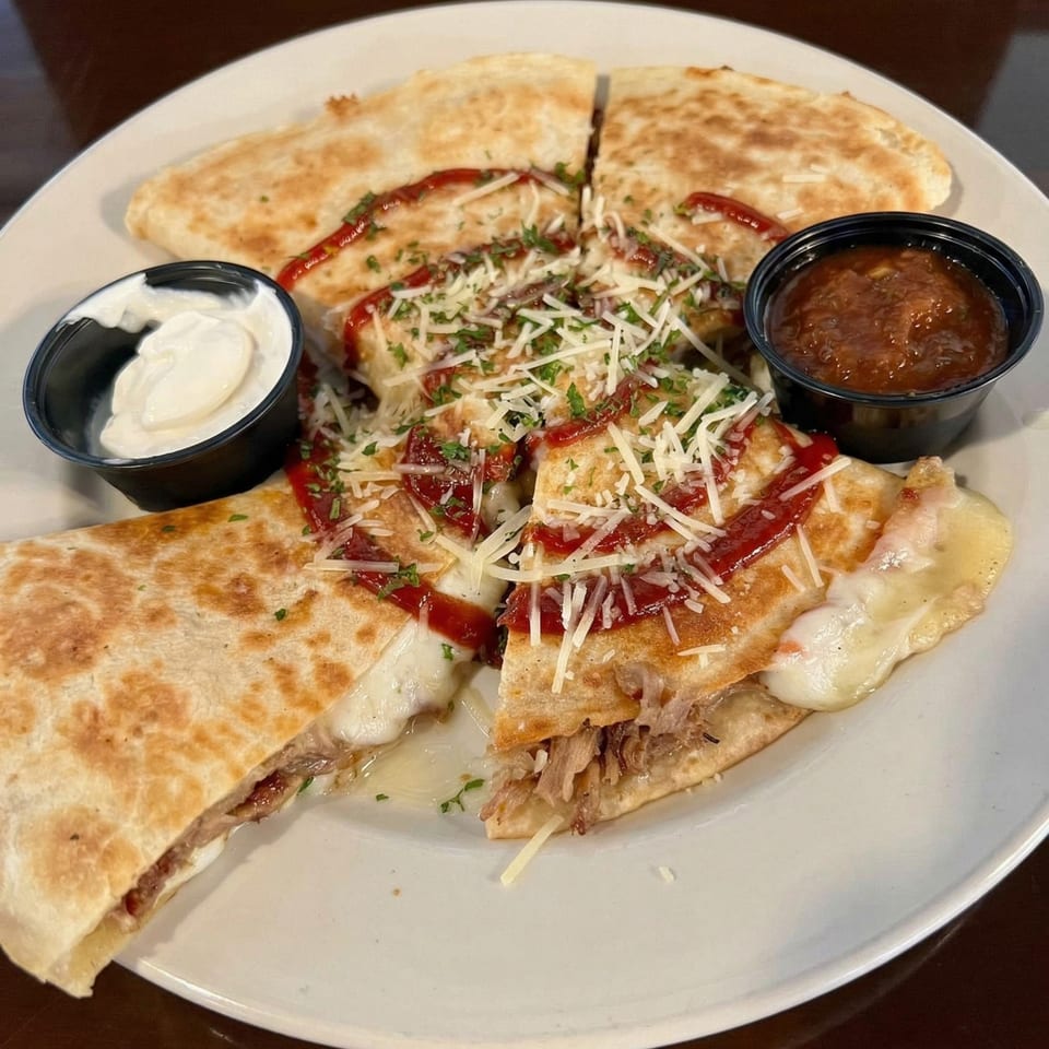 Pulled pork quesadilla with melted cheese, drizzled with sauce, and served with sour cream and salsa.