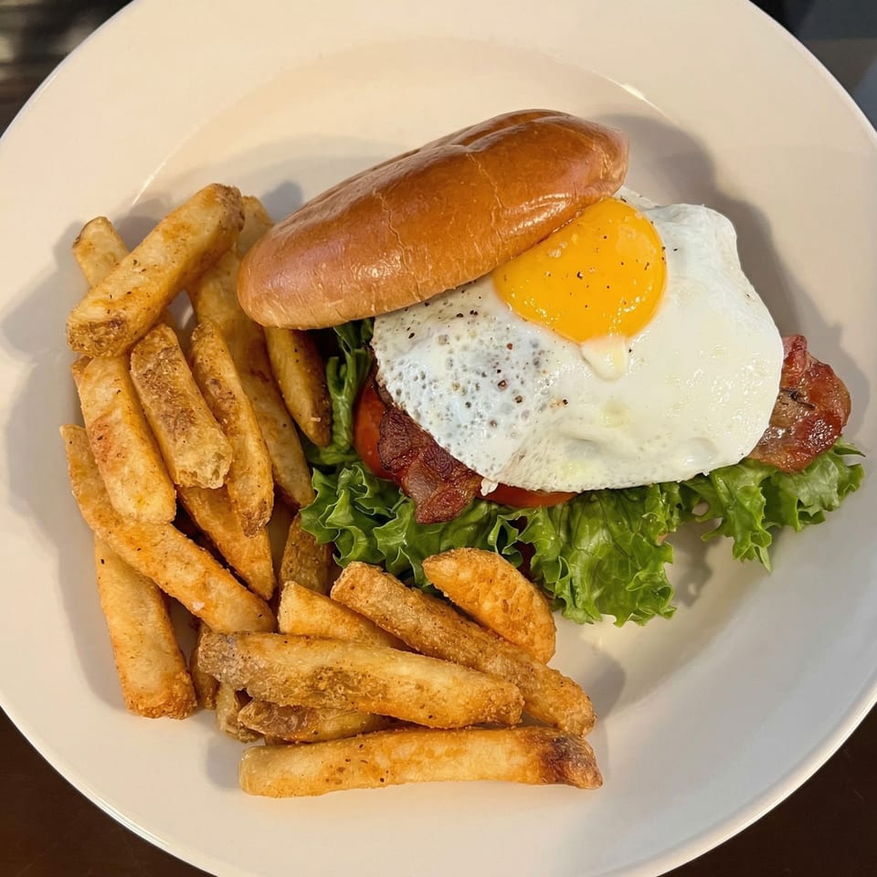 A burger with a fried egg, bacon, lettuce, and tomato, served with a side of fries.