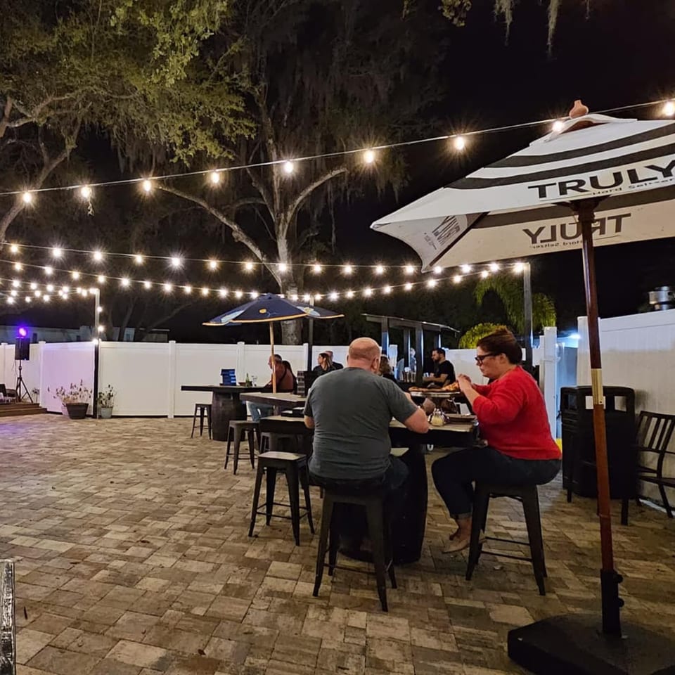 Patrons enjoying the outdoor patio at Whiskey Kitchen Mount Dora at night, illuminated by string lights.
